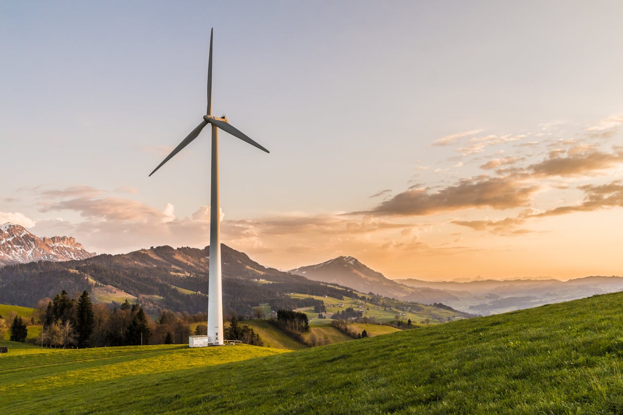 Wind turbine amid rolling hills and mountains at sunset, symbolizing renewable energy and sustainability.